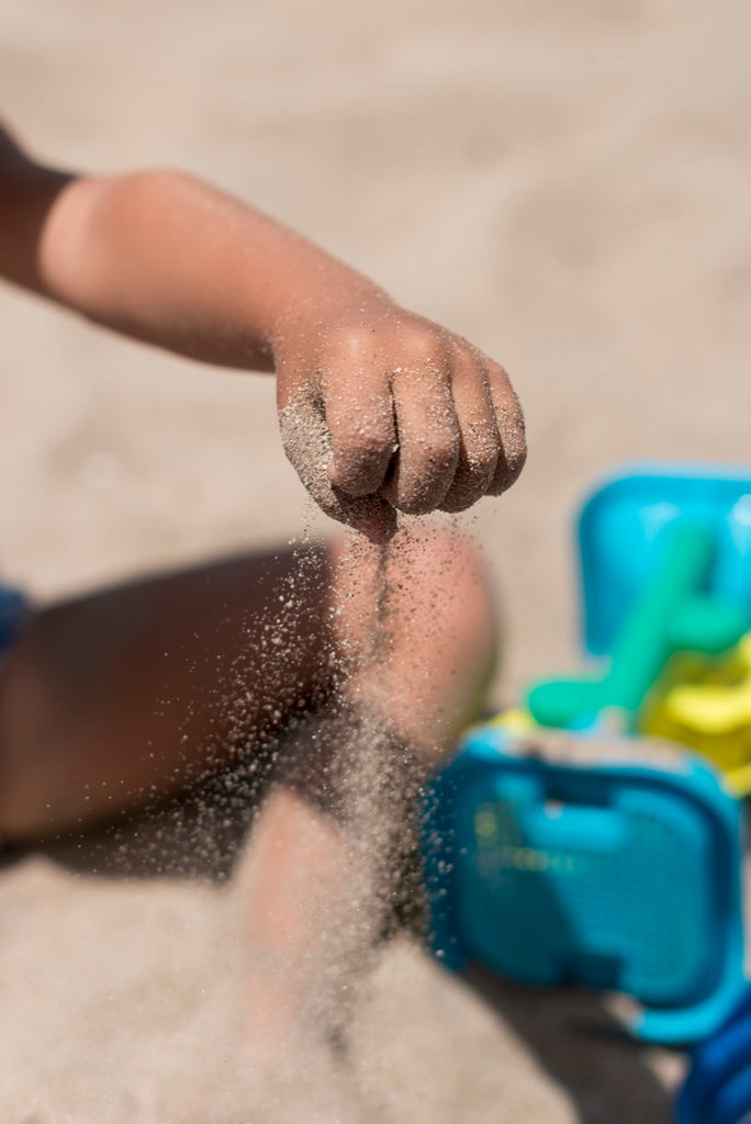 close up kid pouring sand in soft play sand pit